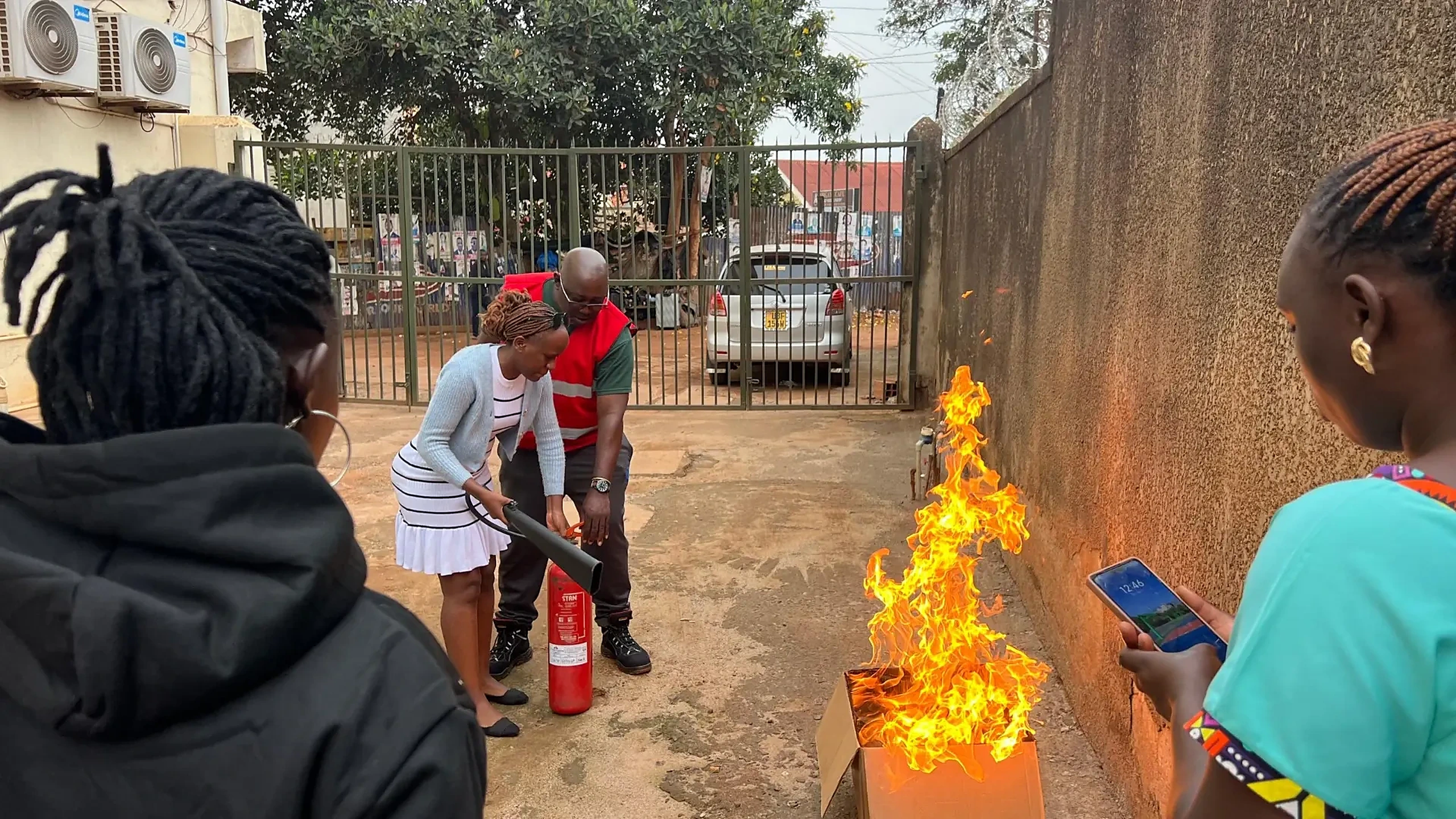 Trainer coaching a participant to discharge a fire extinguisher onto a controlled live fire during firefighting safety training