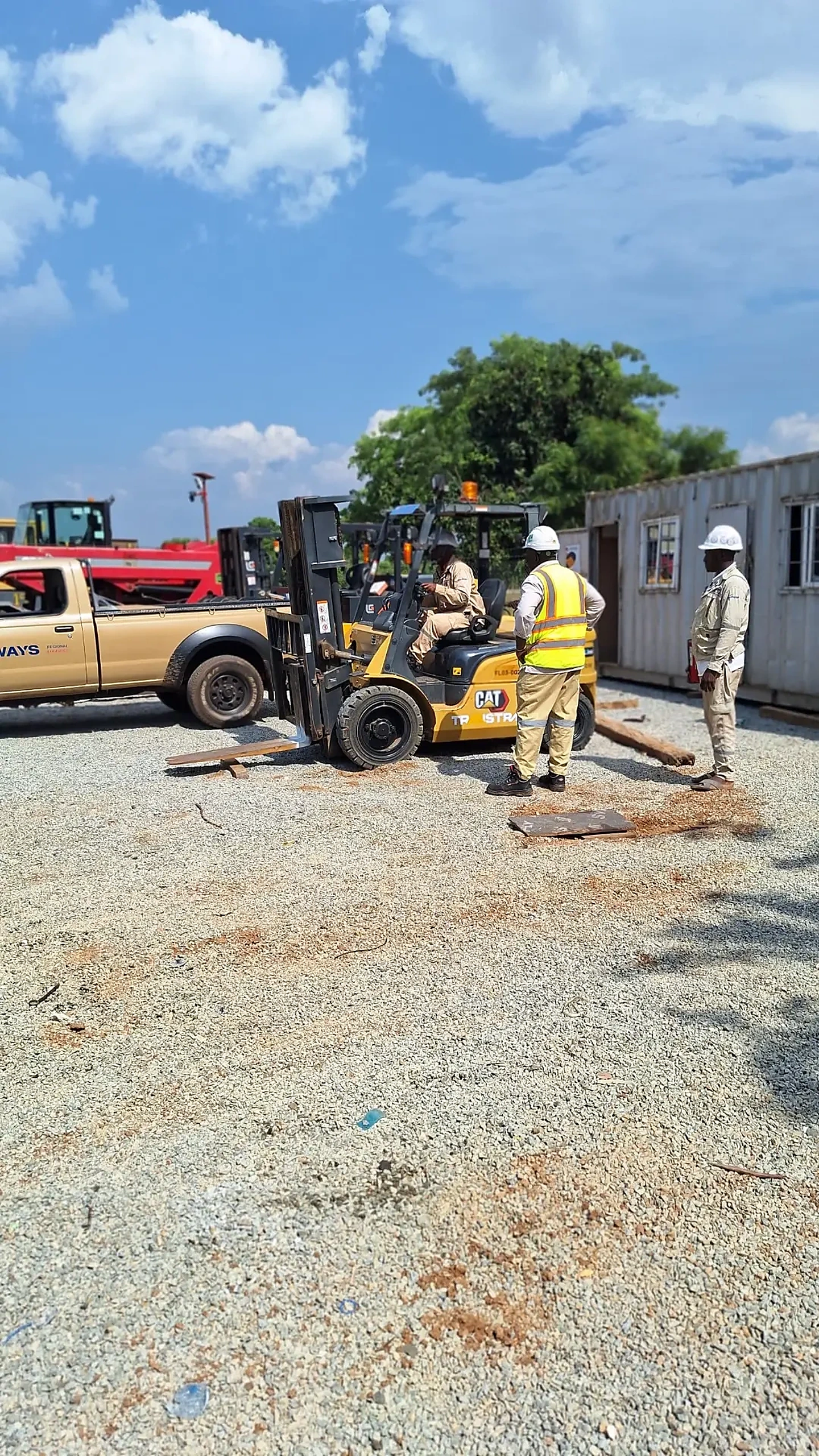 Forklift operator training on a plant yard with a supervisor in a high-visibility vest and a colleague in a hard hat observing