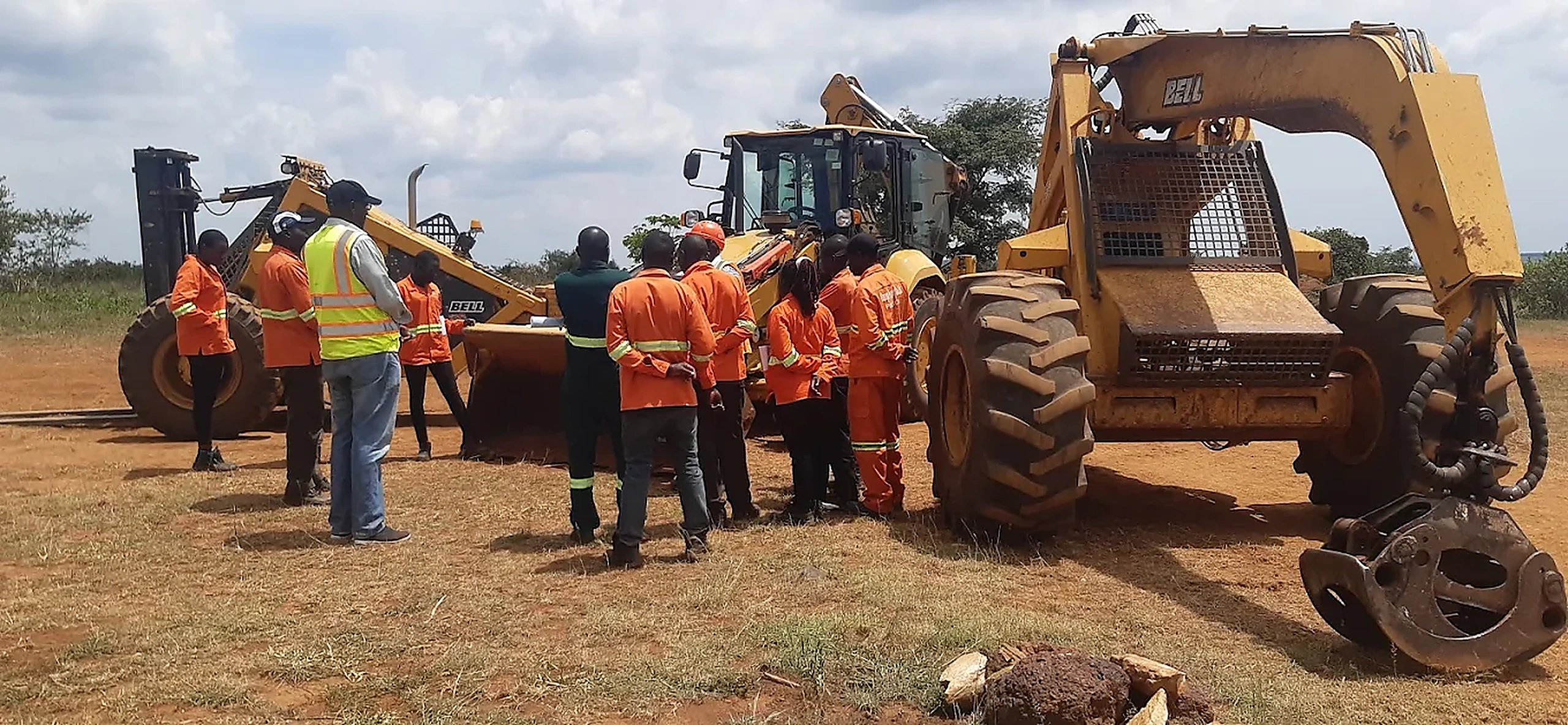 Trainer briefing plant operators in PPE beside a backhoe loader and forklift