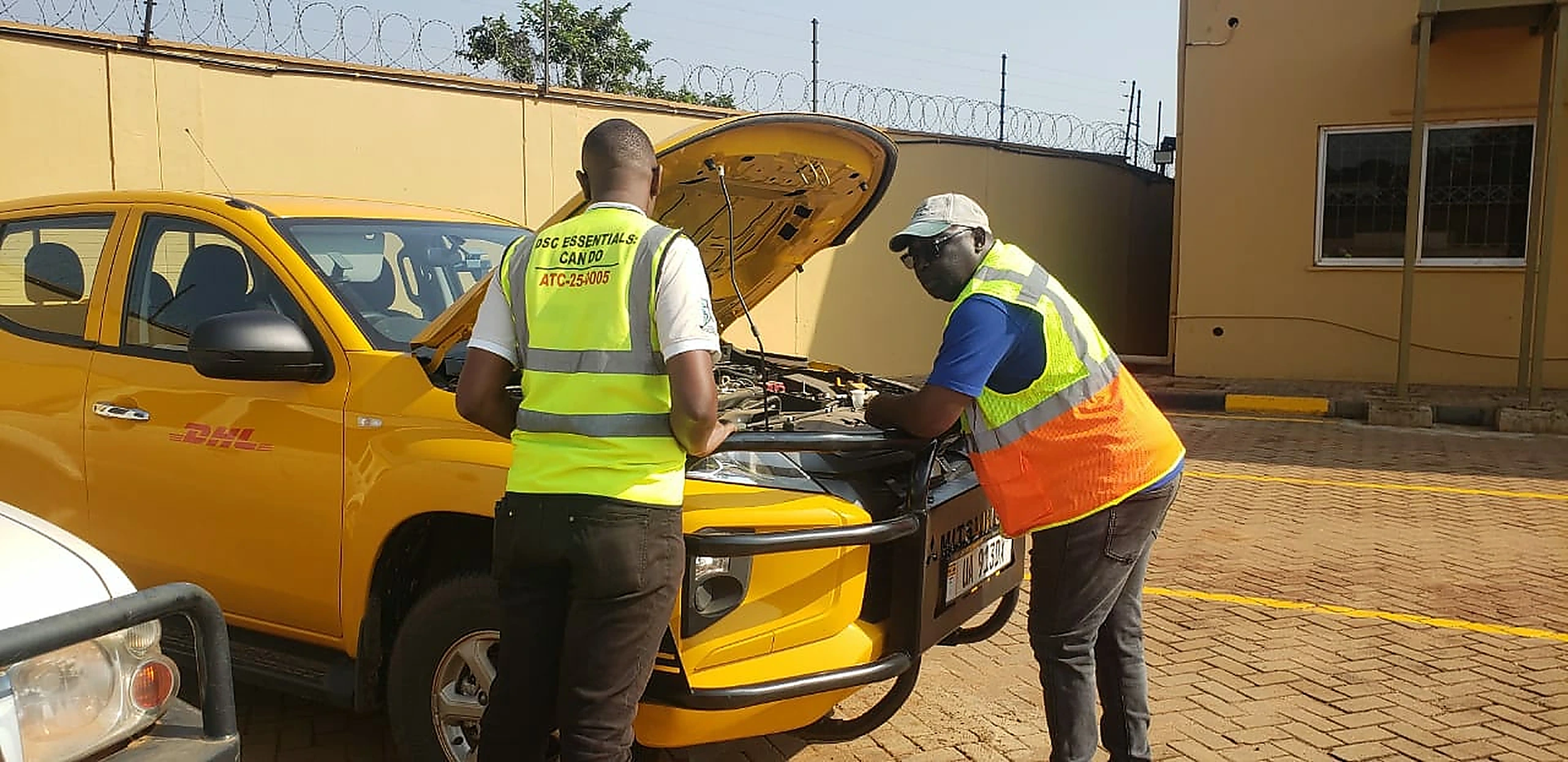 Two drivers in high-visibility vests carrying out a pre-trip engine bay inspection on a company pickup